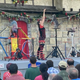 A woman holds a piece of chicken in front of a cat while both are on stage at a Renaissance Faire